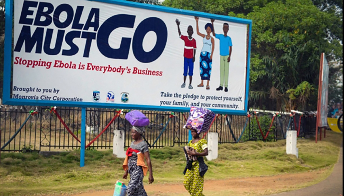 Women walking by a billboarding that says "Ebola must go"
